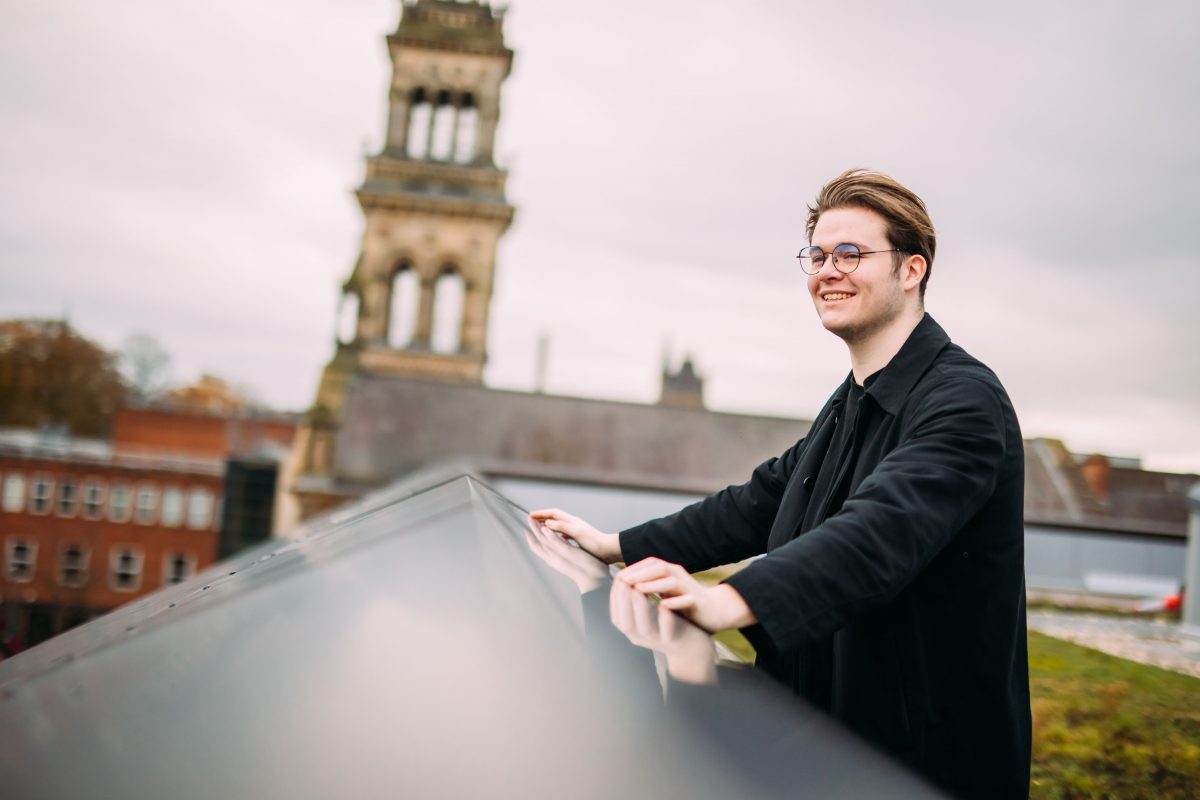 Student smiling, looking out into the distance, on the rooftop of a university building.