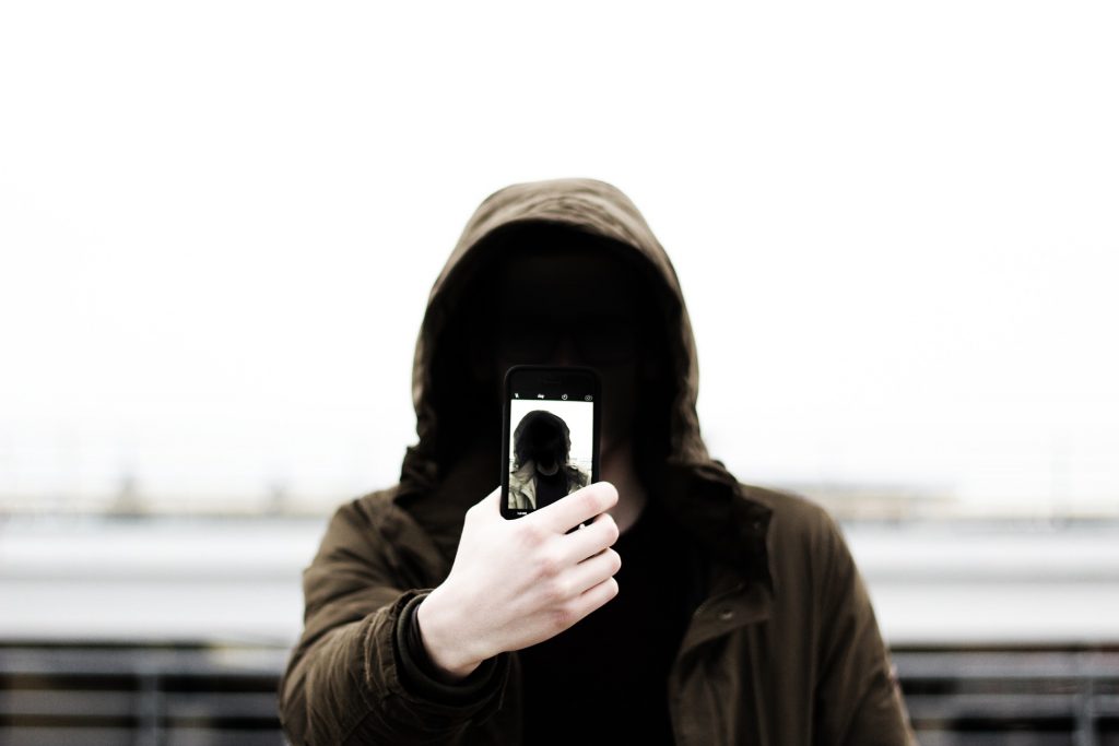 Picture of a person with their face hidden in a hood, taking a selfie.
