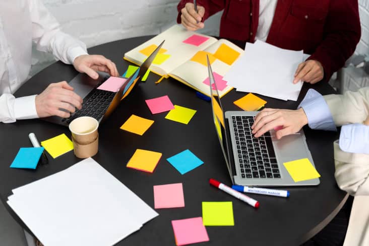 People collaborating on a project, multiple laptops and sticky notes on a desk