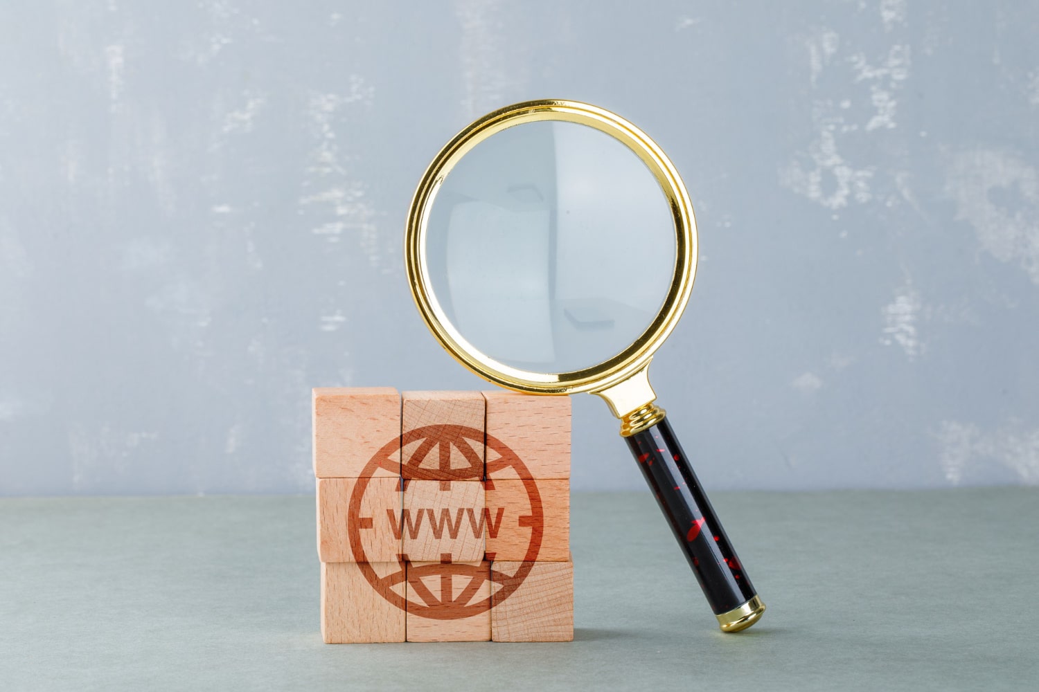 Magnifying glass leaning on a wooden block with a globe and WWW imprinted on it