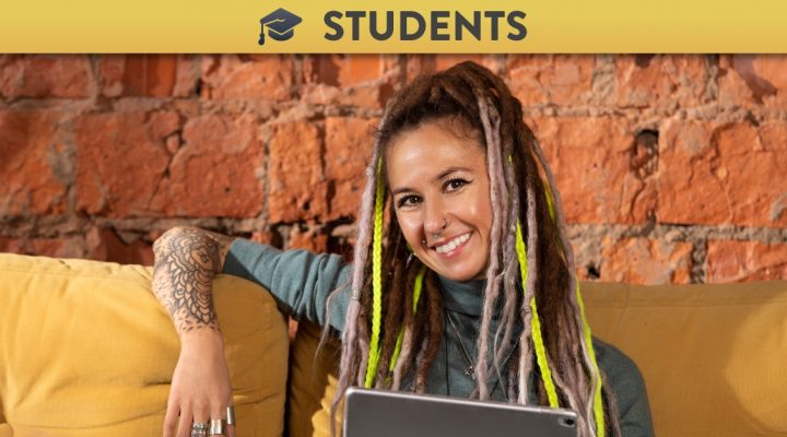 Young female student sitting with laptop, smiling - front view. Yellow tips in long hair