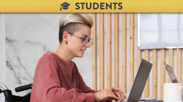 Woman with short hair and glasses in a wheelchair using a laptop