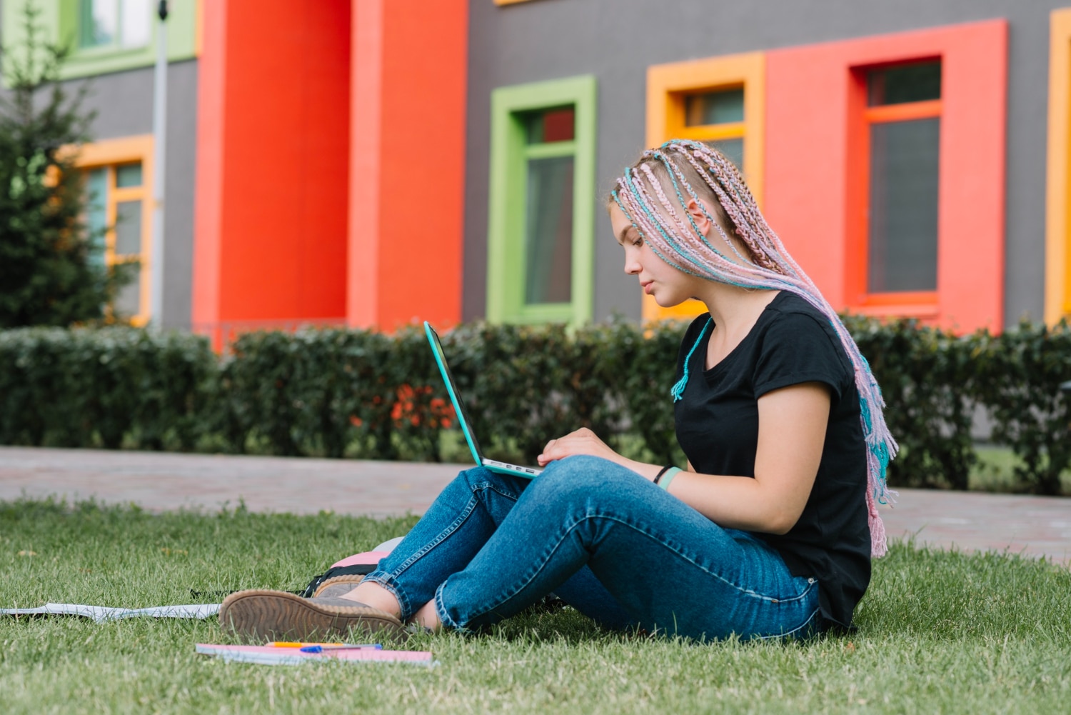 Female student with dreadlocks in park working on laptop