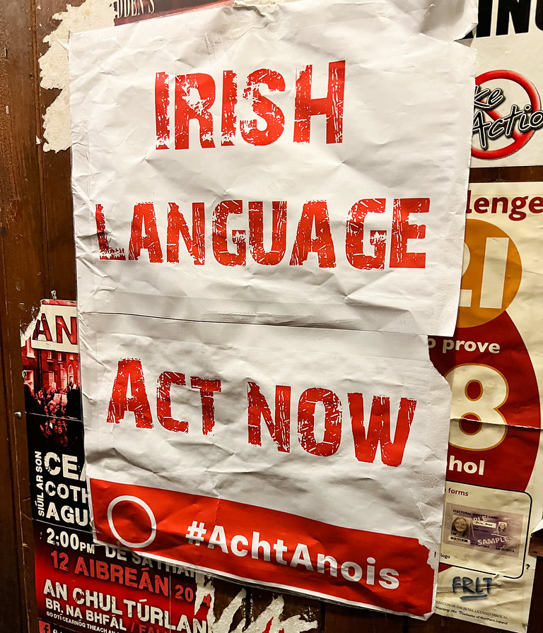 A crumpled white poster reading, in red all caps text, "Irish Language Act now #AchtAnois"