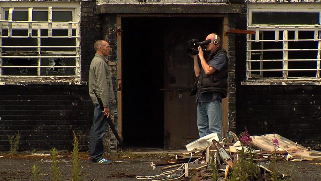 William Mitchell outside a Nissen hut in 2007, being recorded by Paddy Stevenson.