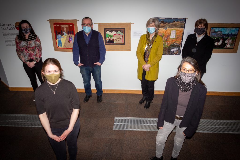 People facing camera with masks on with exhibition in the background. 