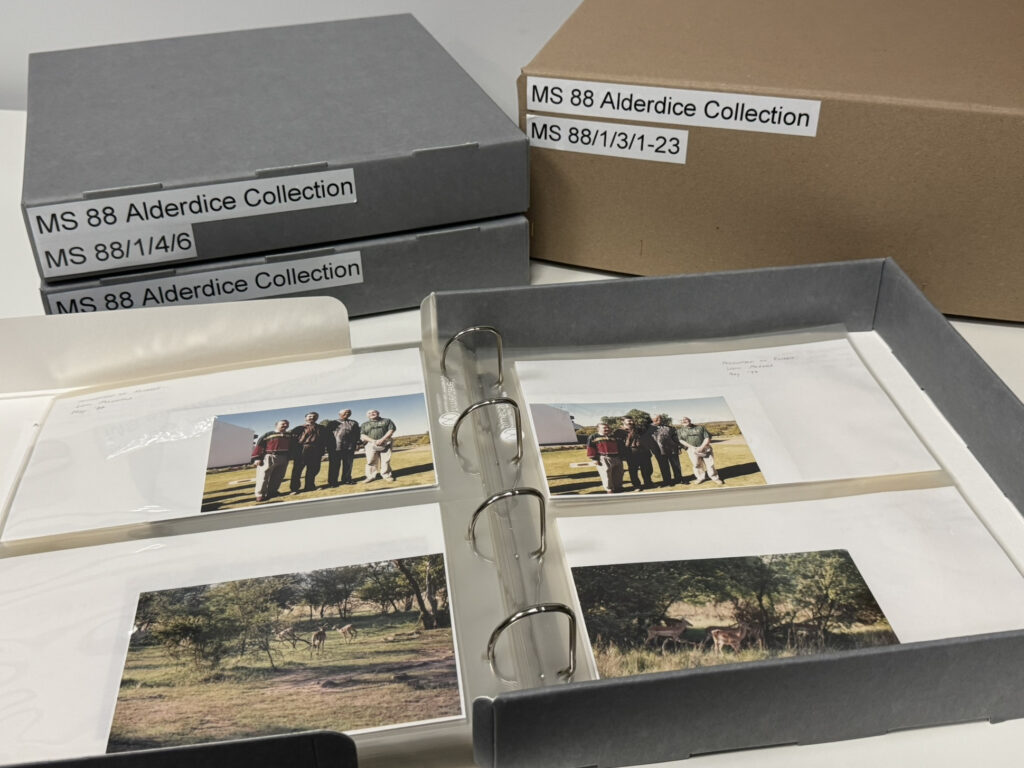 Photograph of archival boxes and photo albums labelled "MS 88 Alderdice Collection". An open archival album shows photographs of Lord Alderdice's visit to South Africa in May 1997, including images of wildlife and a meeting with Nelson Mandela.